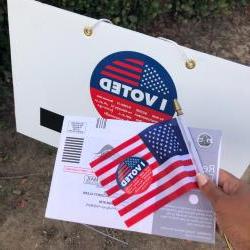 A person holds up an "I Voted" sticker, along with their ballot.